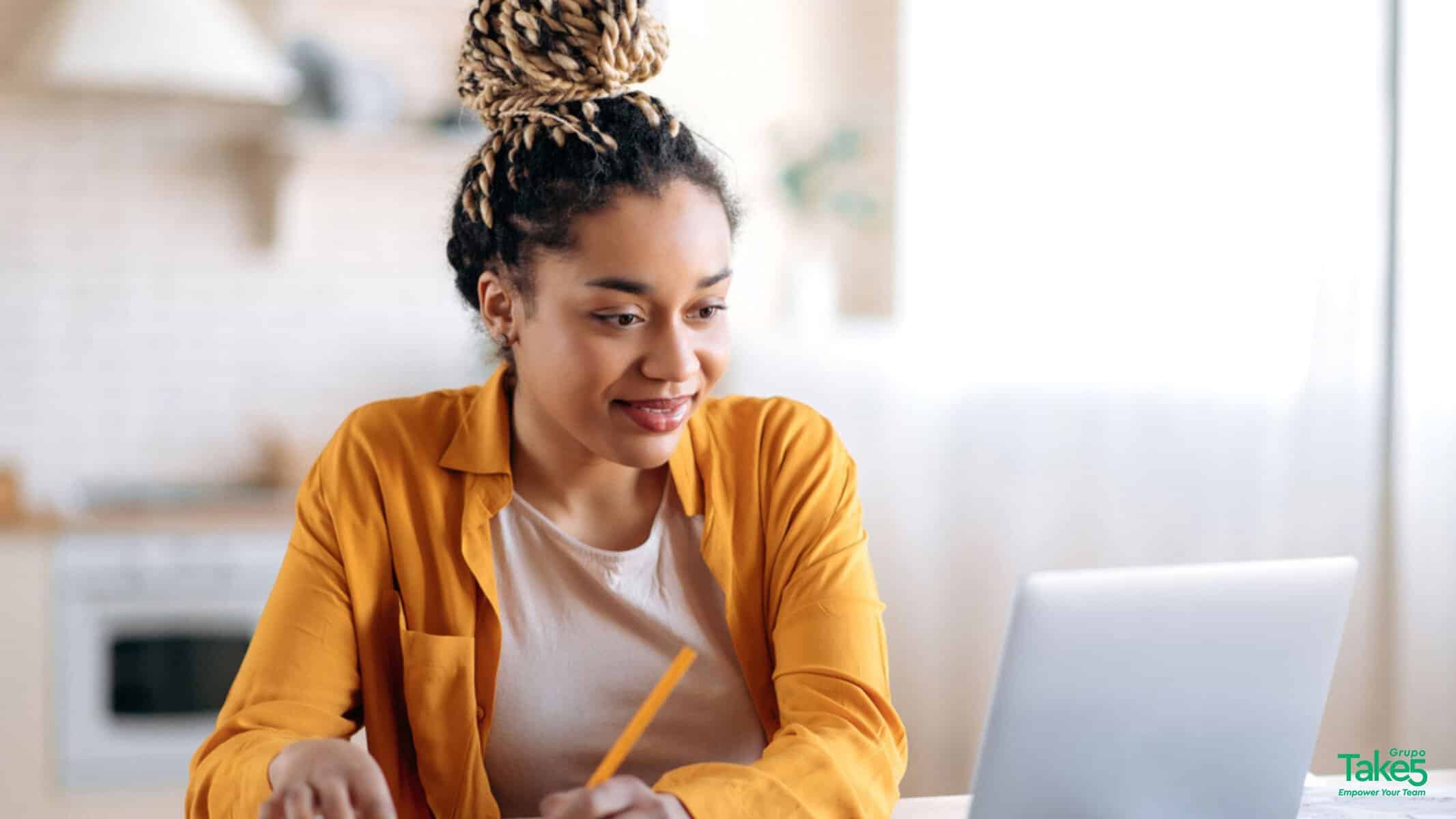 Mulher sentada à mesa em ambiente doméstico, usando notebook e fazendo anotações, representando estudo, trabalho remoto, aprendizado digital e desenvolvimento profissional em home office.