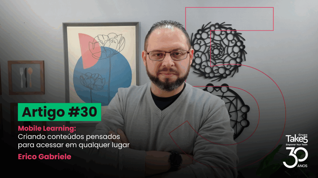 Homem de braços cruzados em ambiente interno corporativo, usando óculos e blusa cinza, em frente a quadros decorativos na parede. À esquerda, texto em destaque: ‘Artigo #30 – Mobile Learning: Criando conteúdos pensados para acessar em qualquer lugar – Érico Gabriele’. À direita, identidade visual do Grupo Take5 com selo de 30 anos.