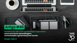 Vista superior de mesa de trabalho com notebook, café e materiais de escritório, ilustrando organização da aprendizagem em plataformas LMS e LXP para educação corporativa, com identidade visual do Grupo Take 5.