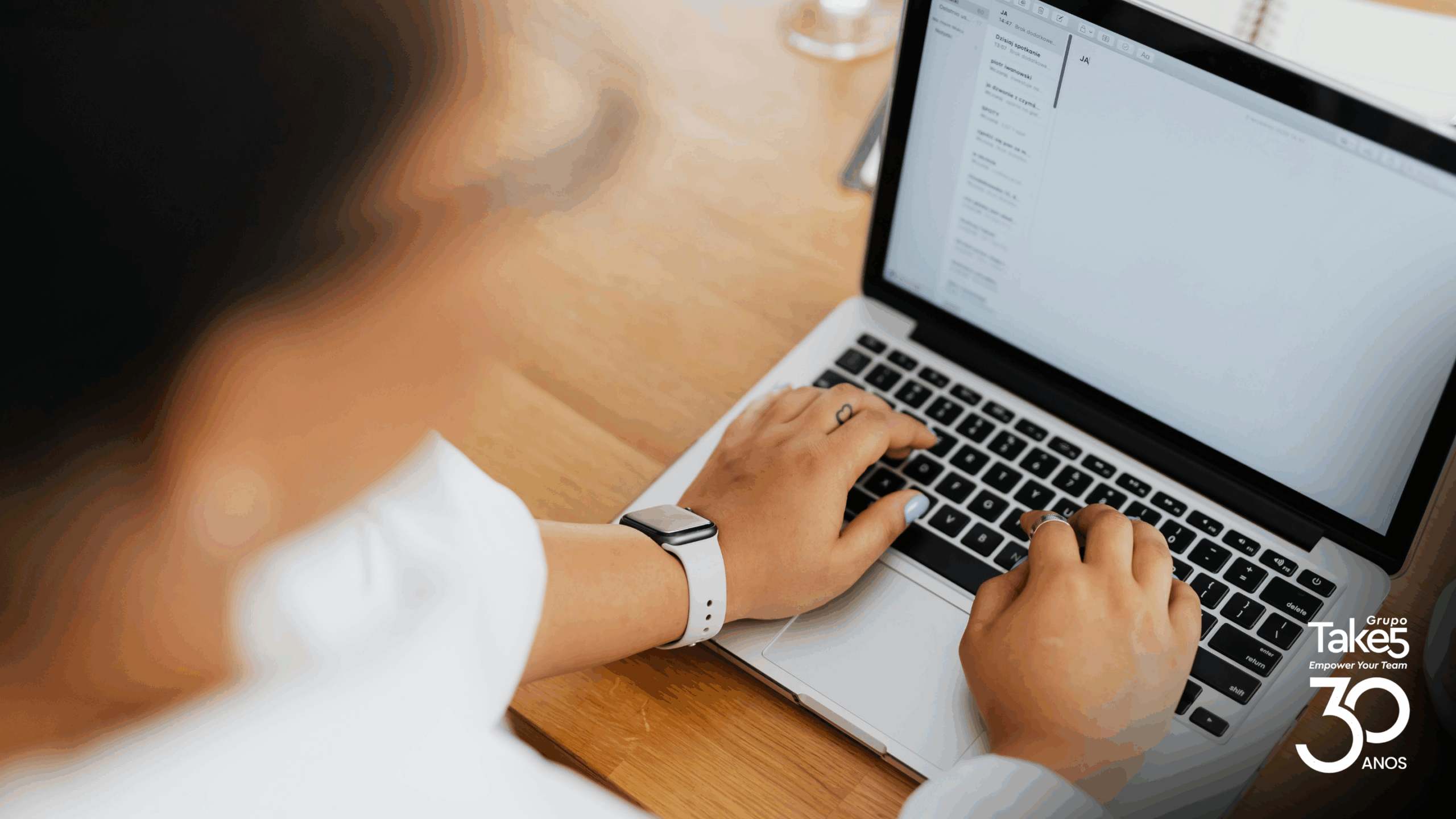 Profissional digita em notebook sobre mesa de madeira, representando produção de conteúdo, aprendizagem digital e uso de tecnologia na educação corporativa do Grupo Take 5.