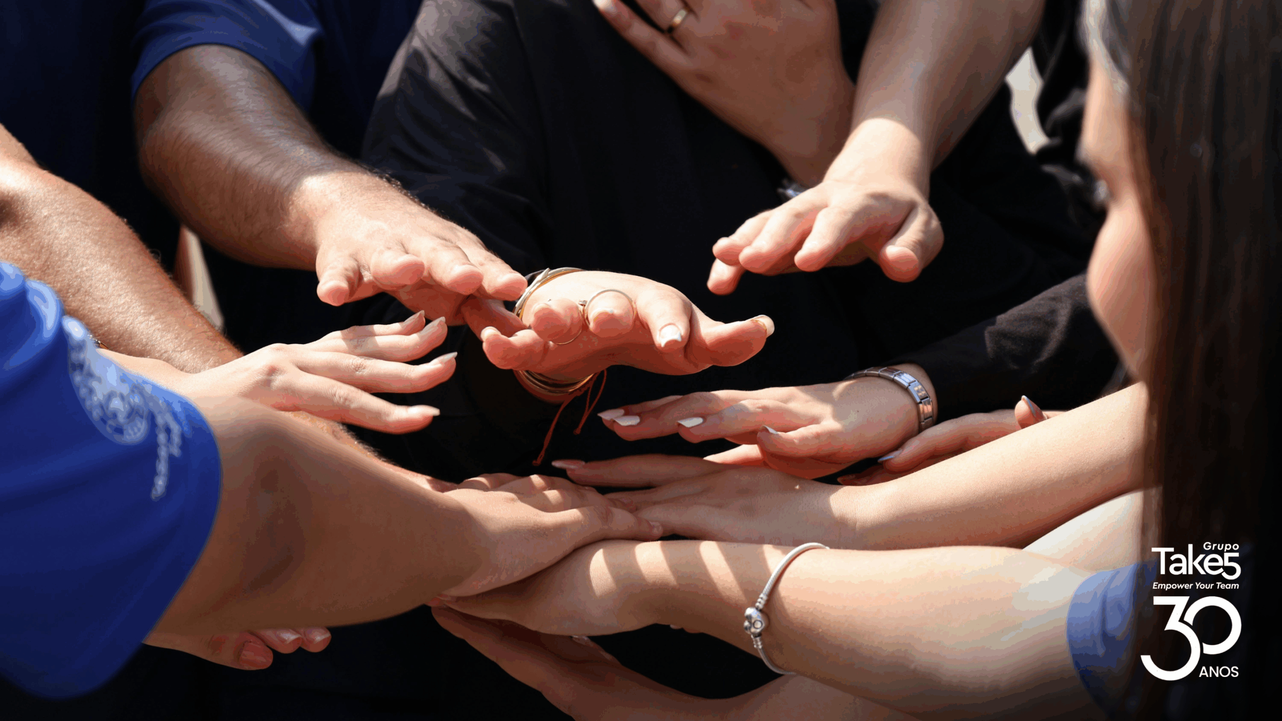 Mãos de várias pessoas reunidas em gesto de união e apoio, simbolizando engajamento, colaboração e trabalho em equipe em iniciativas de educação corporativa do Grupo Take 5.