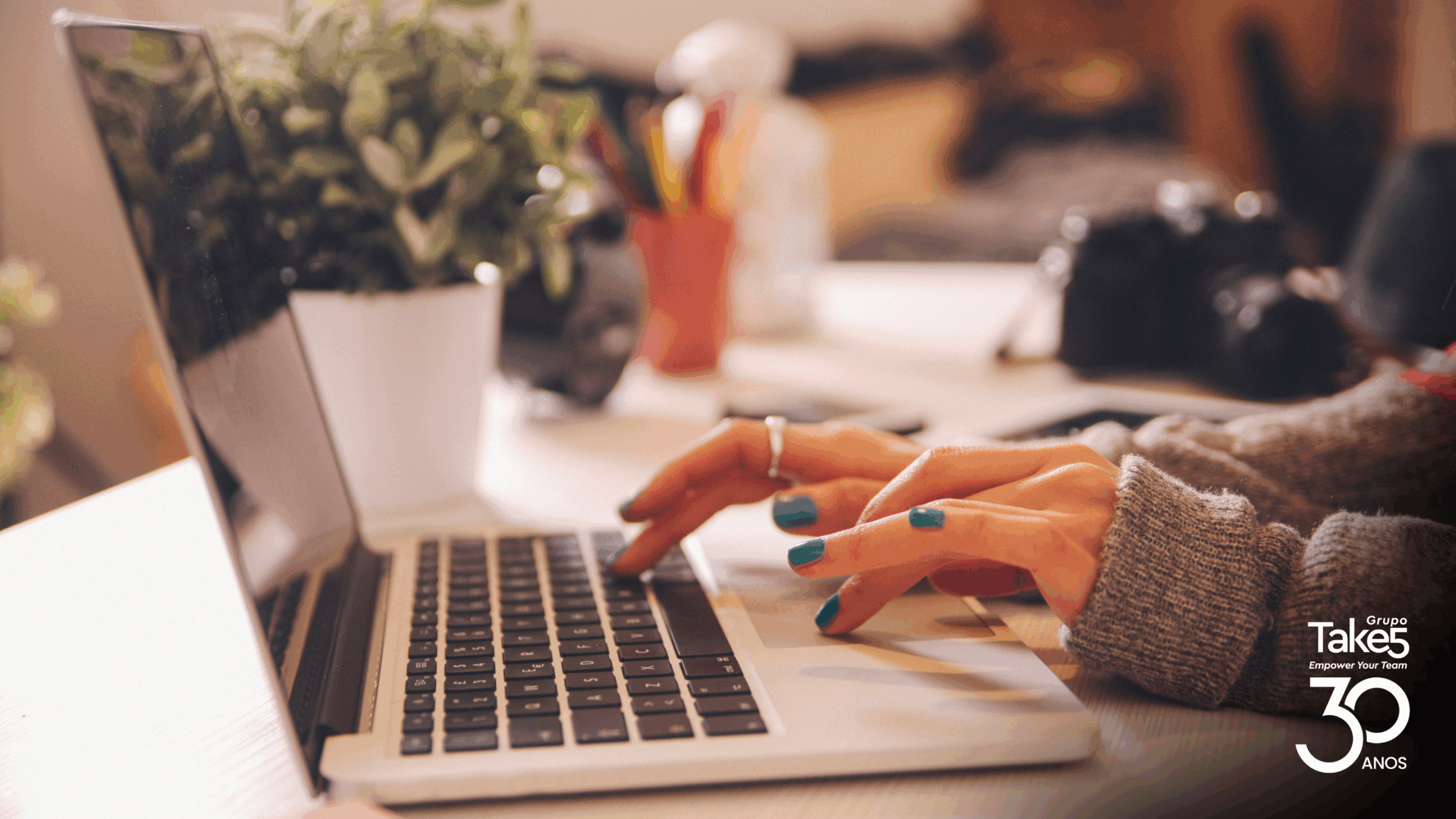 Pessoa digitando em notebook em ambiente de trabalho aconchegante, representando produção de conteúdo, aprendizagem digital e uso de tecnologia em educação corporativa do Grupo Take 5.