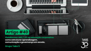 Vista superior de mesa de trabalho com notebook, café e materiais de escritório, ilustrando organização da aprendizagem em plataformas LMS e LXP para educação corporativa, com identidade visual do Grupo Take 5.