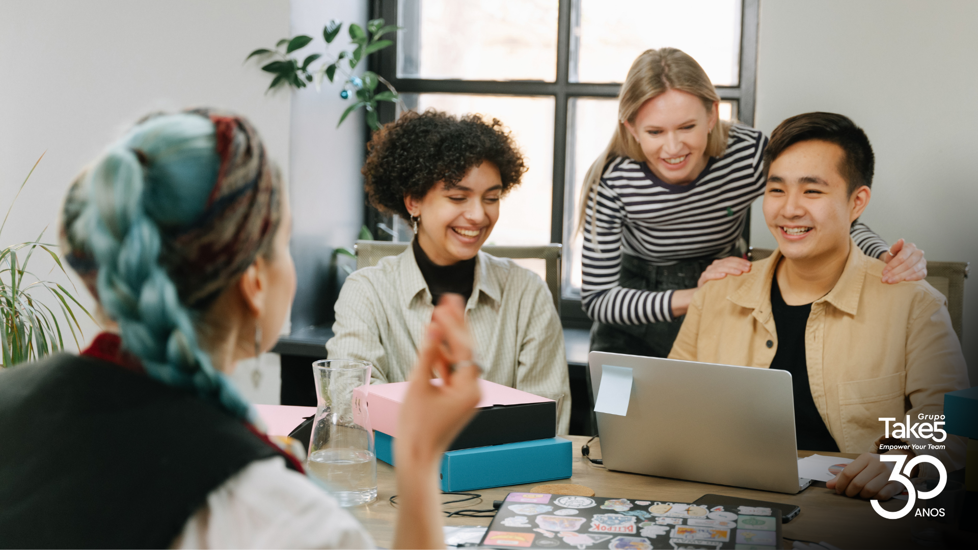 Grupo de colaboradores colaborando em torno de um notebook, demonstrando engajamento e trabalho em equipe.